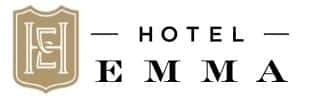 Logo of Hotel Emma with a brown and white emblem on the left side featuring intricate designs and the letters "H" and "E". To the right, the text "HOTEL" is written in uppercase with horizontal lines on either side, and "EMMA" is written below in larger uppercase letters.