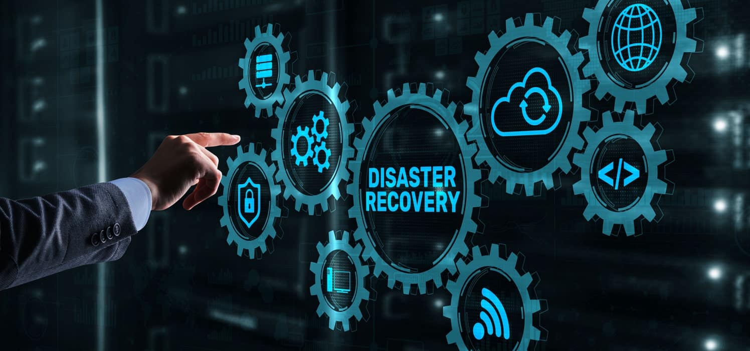 A hand pointing towards interlocking gears with icons on them, including a cloud, globe, shield, wifi, and coding symbols. The central gear has the text "DISASTER RECOVERY" written on it, representing a concept of integrated disaster recovery solutions and technology.