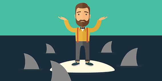 A bearded man wearing an orange shirt, gray pants, brown suspenders, and blue sneakers stands on a small white island, raising his hands in a confused gesture. Shark fins circle the island in the dark water, against a teal background.